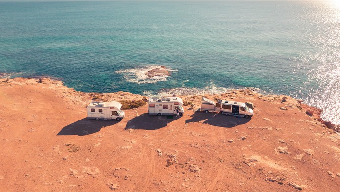 3 RVs sit on the edge of an arid cliff overlooking the ocean