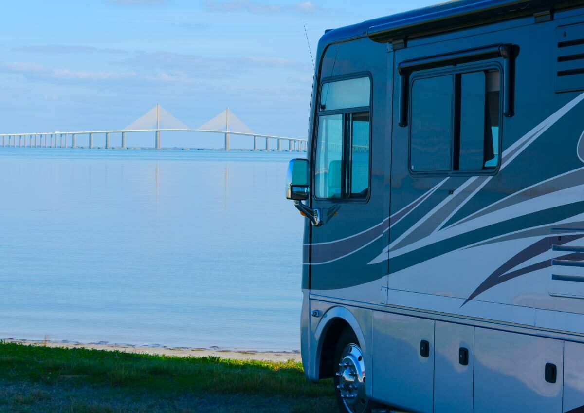An RV parked near the water with the Skyway Bridge of Tampa Bay, FL, in the background.