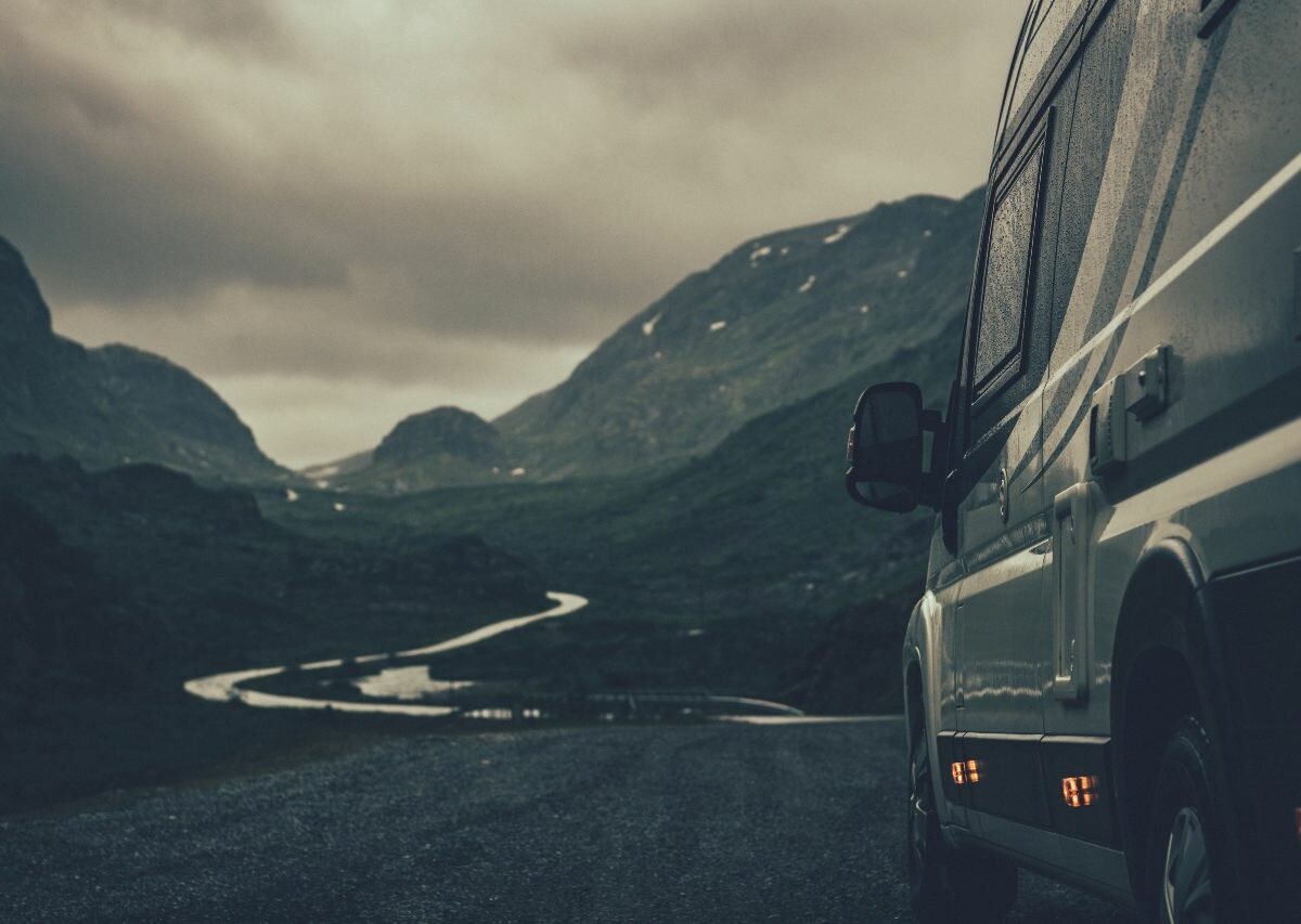 RV is on a winding road, headed into a valley during stormy weather.