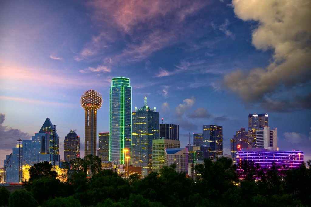 The Dallas skyline is illuminated at dusk by lights on the tall buildings.