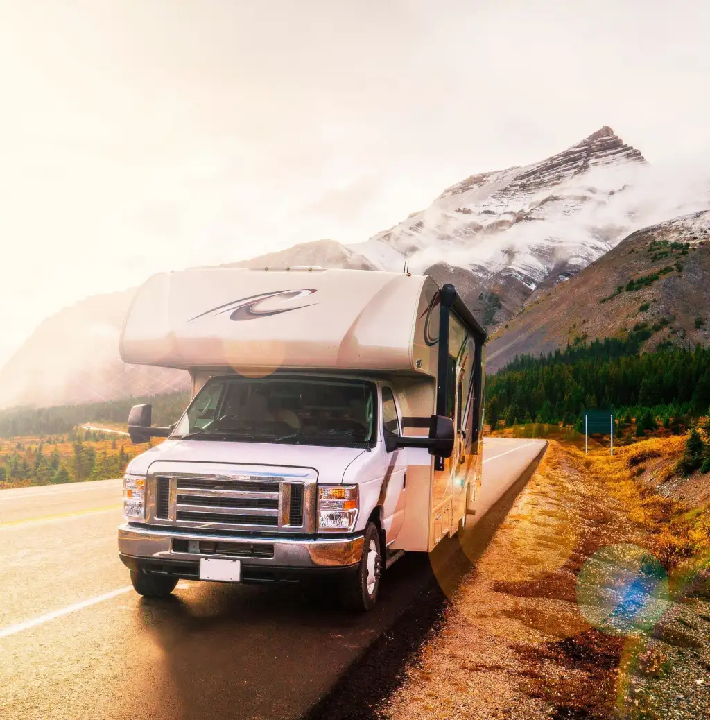 RV parked at sunset on a mountain road with mountains in the background.