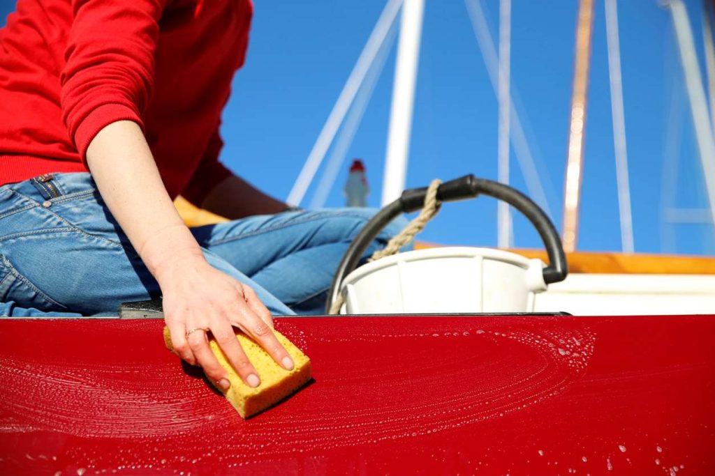 Someone cleaning their red boat with a sponge a soap 
