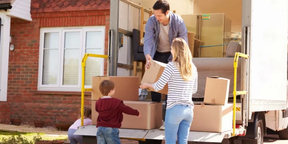 A family of four unpacking a moving truck full of boxes at their new home.
