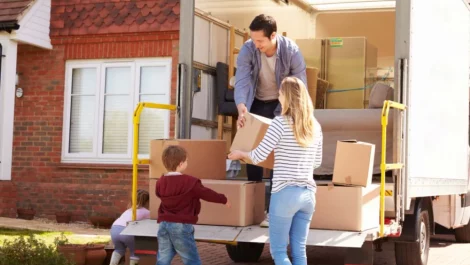 A family of four unpacking a moving truck full of boxes at their new home.