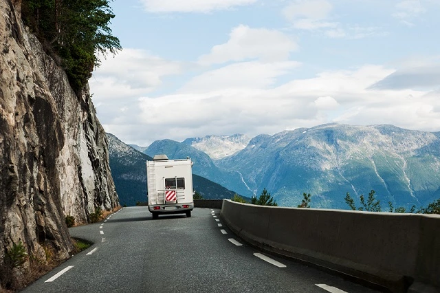 An RV traveling down a road in a beautiful mountainous area.