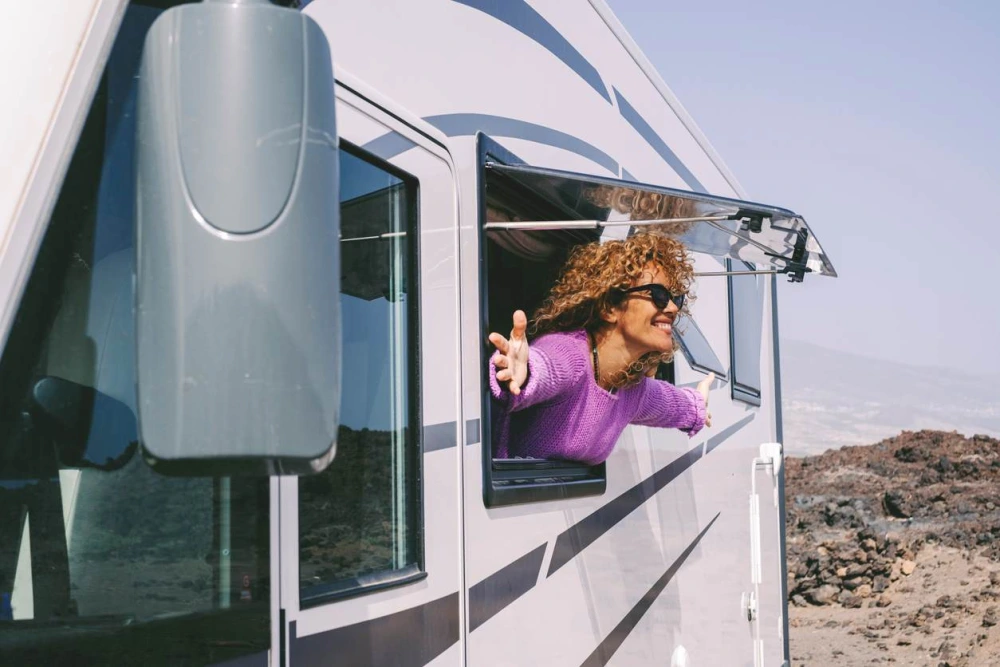 A woman with her head and arms out of the window of an RV