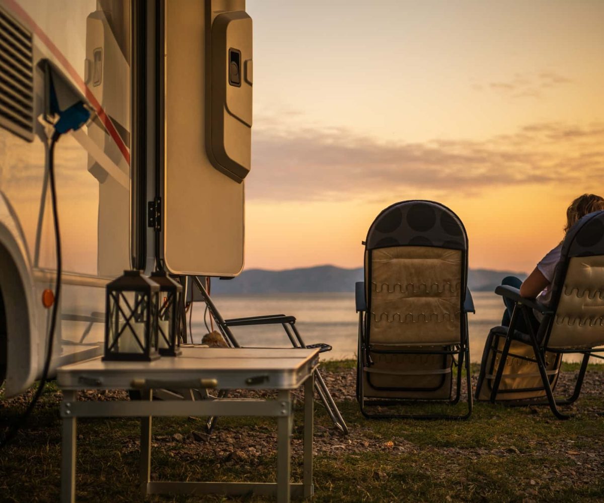 An RV parked lakeside at sunset with a retired couple enjoying the view.