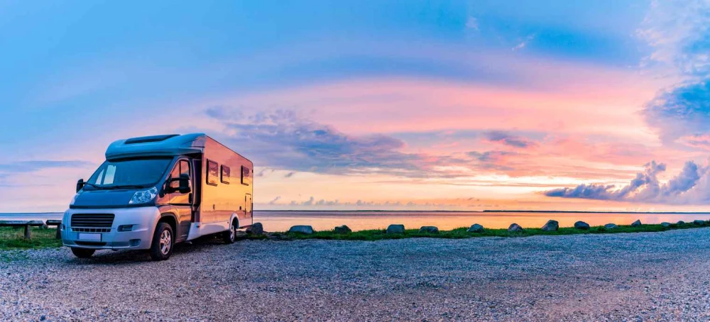 An RV parked next to a lake at sunset