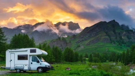 An RV parked on the grass in front of the mountains