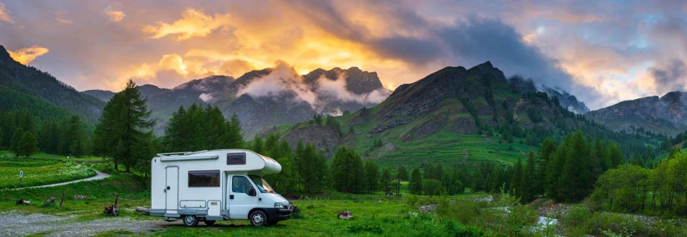An RV parked on the grass in front of the mountains