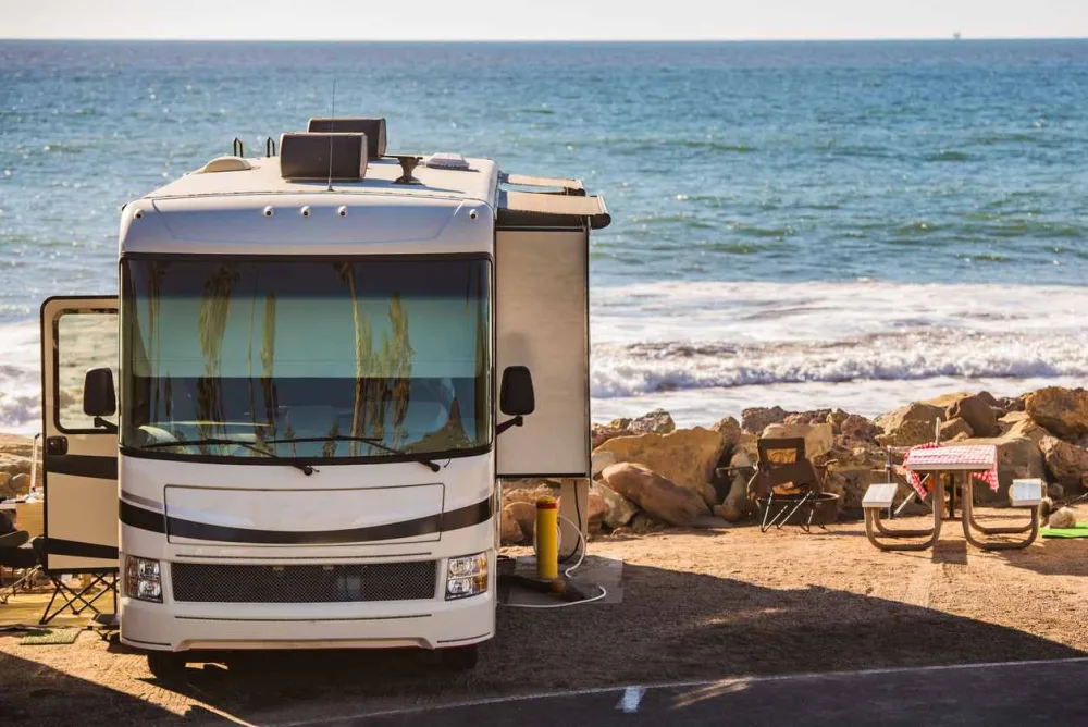 An RV set up with a picnic table on the lake beach