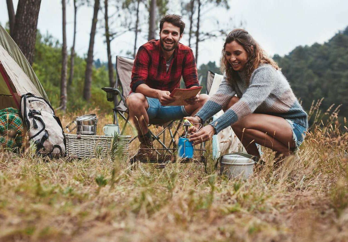 A young man and woman smiling while camping in nature.