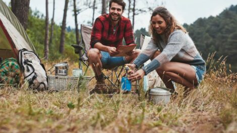 A young man and woman smiling while camping in nature.