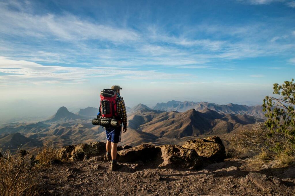 A solo hiker stands atop a cliff overlooking the Mexican border in Big Bend National Park, TX.