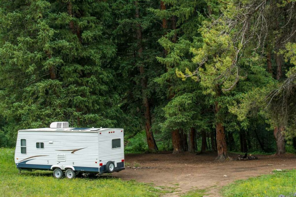 A view of a camper sitting on the edge of a woodsy area.